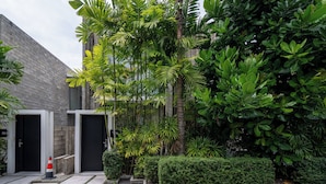 A modern building with a concrete facade, a gated entrance, and a well-maintained garden with various tropical plants. - Oceanphere Villa by Prop Hopper (Sattahip)