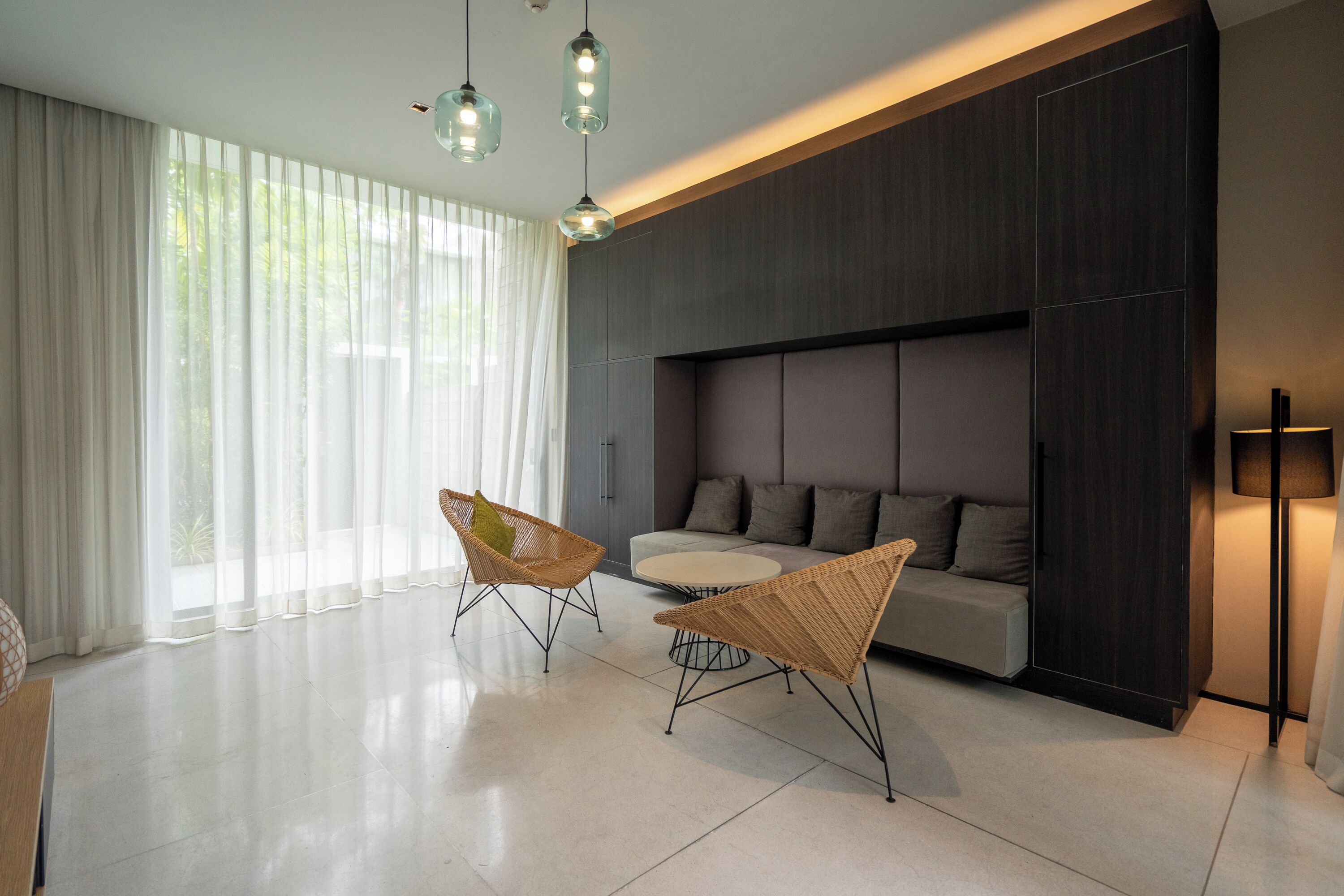 A modern living room with a sofa, two wicker chairs, a coffee table, and a large window with sheer curtains.