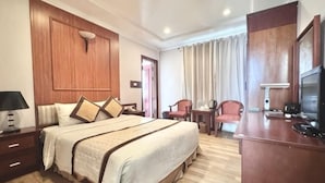 Une chambre d’hôtel avec un grand lit, un bureau, une chaise, une télévision et une tête de lit en bois.