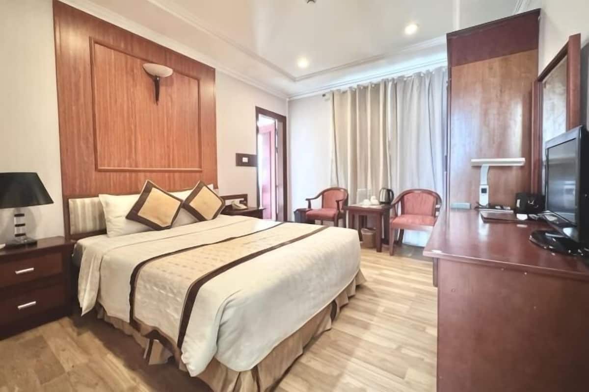 Habitación de hotel con una cama grande, un escritorio, una silla, un televisor y un cabecero de madera.