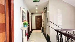 Un couloir d’hôtel avec un plancher en bois, un mur blanc orné d’un tableau encadré, une plante en pot et un escalier avec une rampe en métal.