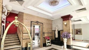 Un hall d’hôtel avec un grand escalier, un comptoir d’accueil et un lustre.
