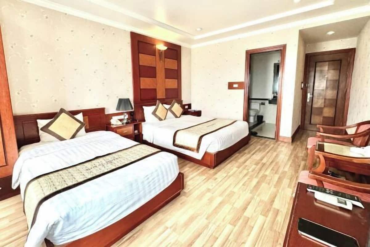 Habitación de hotel con dos camas, piso de madera, un escritorio con silla y una puerta que da a un baño.