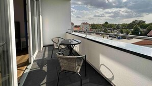 En balkon med gelænder af glas, to fletstole og et lille bord.