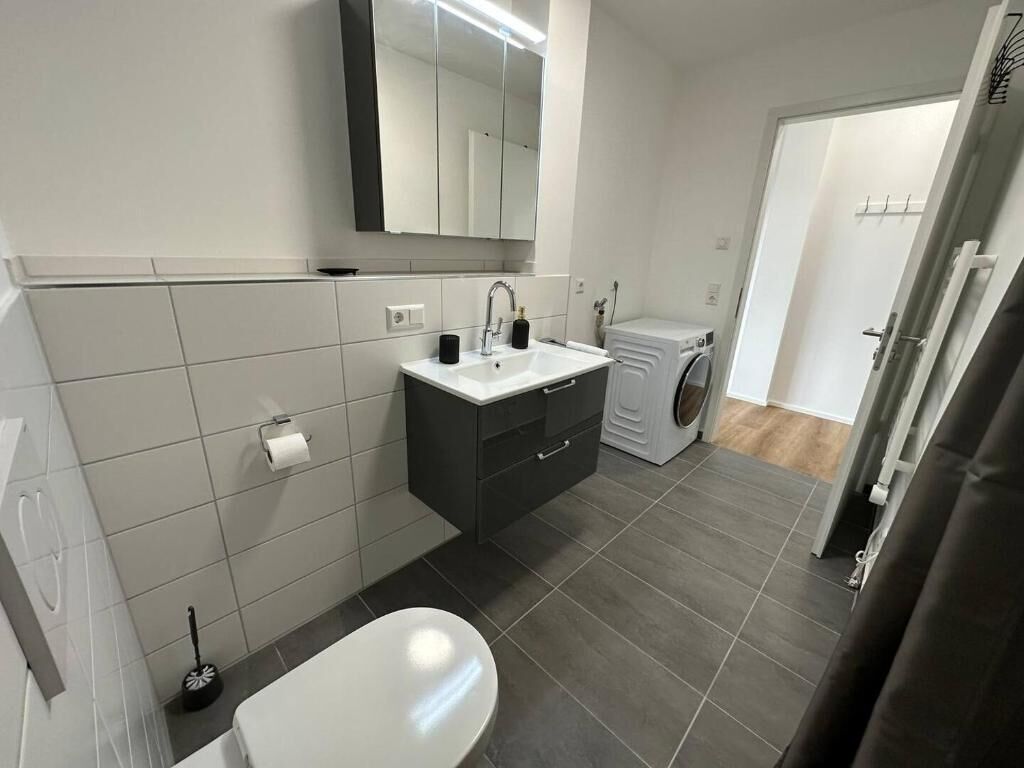 Ein modernes Badezimmer mit einem weißen Waschbecken, dunklen Schränken, einem Spiegel, einer Toilette und einer Waschmaschine.
