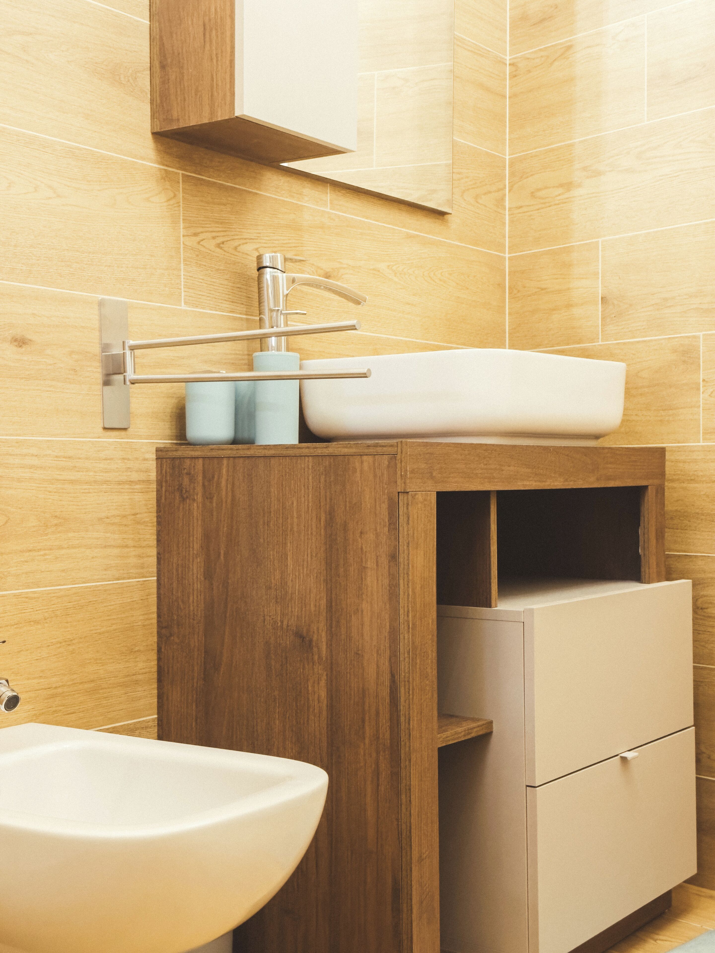 Un baño con tocador de madera, lavamanos y espejo.