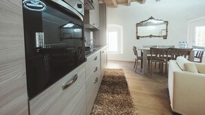 A modern kitchen with a built-in oven, a dining area with a wooden table and chairs, and a large mirror above the table. - Casa da Victoria - Apartment 3 (Castrezzato)