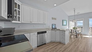 A modern kitchen with white cabinetry, a dishwasher, and a dining area with a view. - Oceanfront Retreat, Private Beach, Stunning Views (North Topsail Beach)