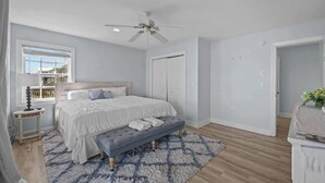A bedroom with a bed, a bench, a ceiling fan, and a window. - Oceanfront Retreat, Private Beach, Stunning Views (North Topsail Beach)