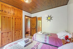 A bedroom with two beds, wooden wardrobes, a ship's wheel decoration, and a bottle of wine on a nightstand.