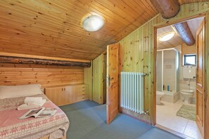 Un dormitorio con paneles de madera, una cama, una puerta que da al baño y un radiador a la vista.
