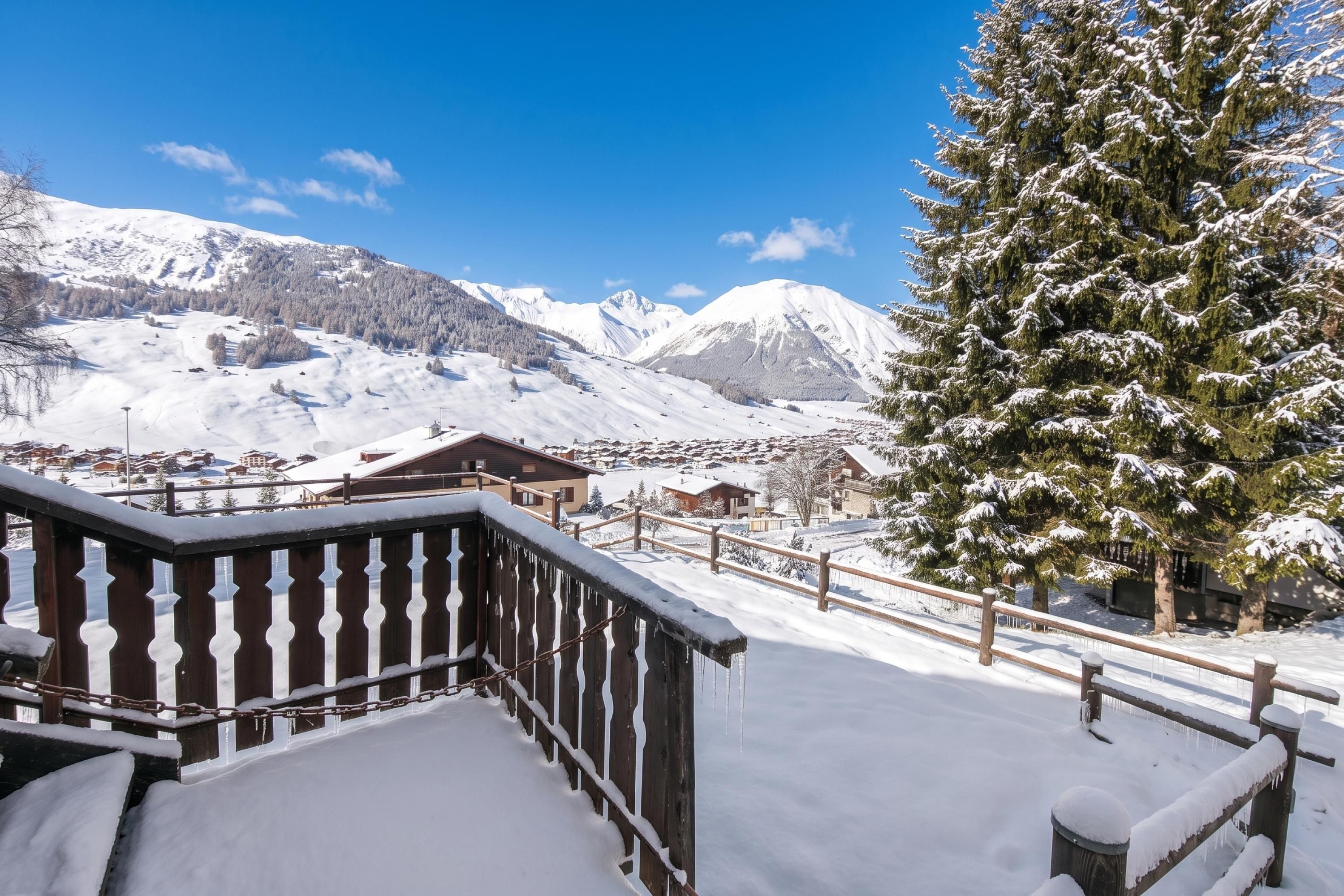 A snow-covered mountain landscape with a wooden fence and a snow-laden tree.