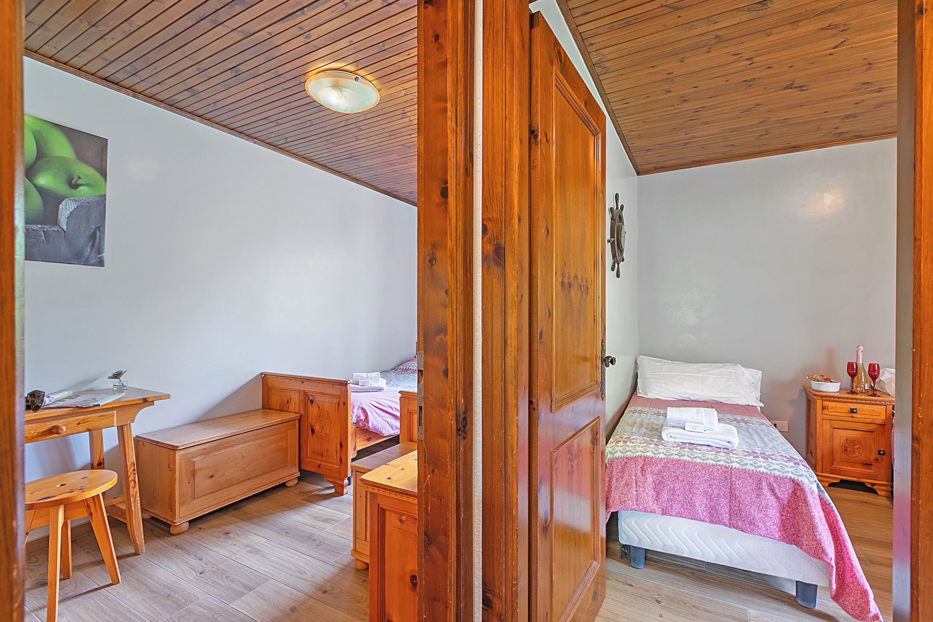 A bedroom with a wooden bed, a desk, a chair, a wardrobe, and a nightstand with a bottle and glasses.