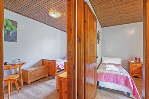 Een slaapkamer met een houten bed, een bureau, een stoel, een kledingkast en een nachtkastje met een fles en glazen.