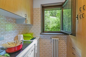 Een keuken met patroontegels, een raam met uitzicht op groen, een rode pan op het fornuis en een groene afwassigheid.