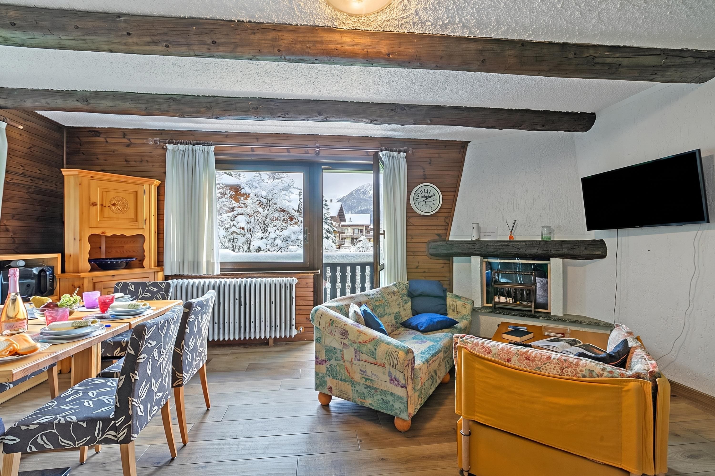 Un salon chaleureux avec un plafond en bois, un coin repas avec une table et des chaises, un canapé et un téléviseur fixé au mur.