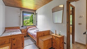A bedroom with two wooden beds, a wooden dresser, a mirror, and a window with a view of greenery.