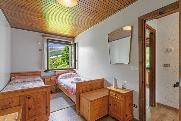 A bedroom with two wooden beds, a wooden dresser, a mirror, and a window with a view of greenery.