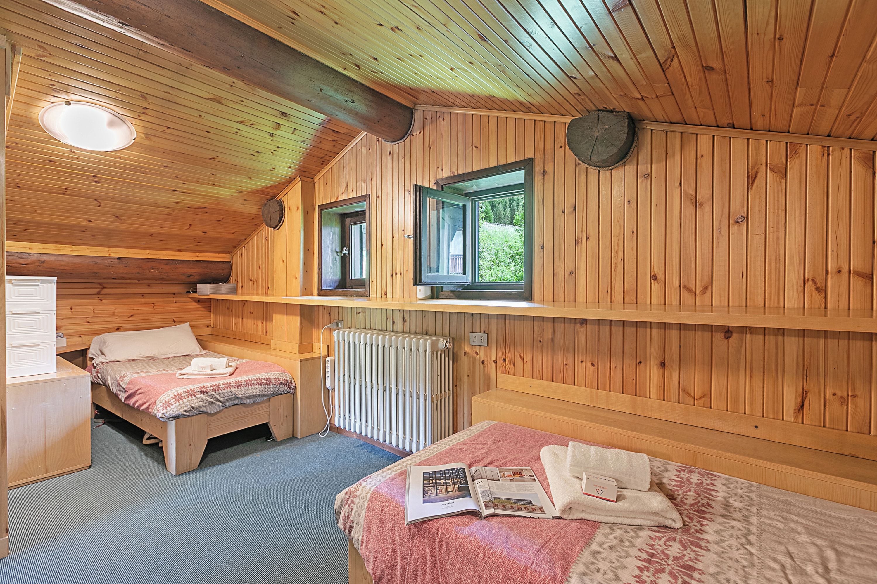 A cozy cabin with two wooden beds, a small desk, and a window with a view of greenery.