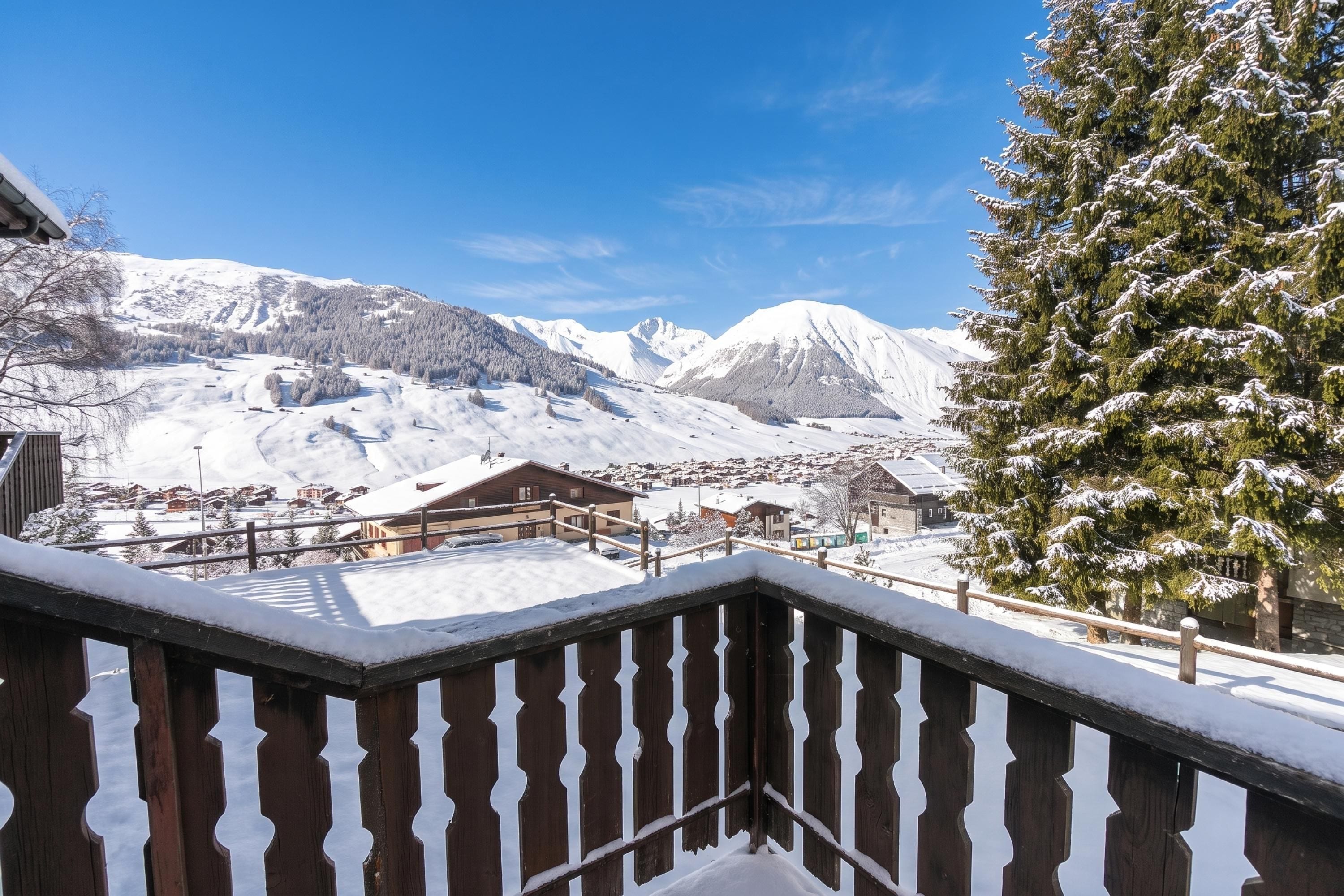 A wooden balcony railing overlooking a snowy mountain landscape with a clear sky.