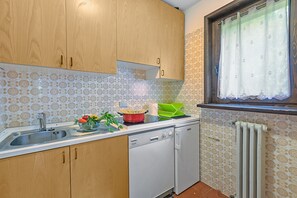 A kitchen with wooden cabinets, a dishwasher, a sink, a window with a curtain, and patterned wall tiles.
