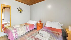 A bedroom with two beds, a wooden ceiling, a ship's wheel decoration, a mirror, and a nightstand with a lamp.
