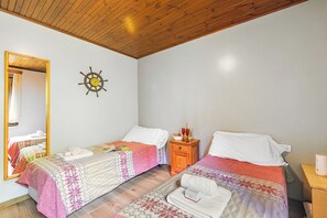 A bedroom with two beds, a wooden ceiling, a ship's wheel decoration, a mirror, and a nightstand with a lamp.