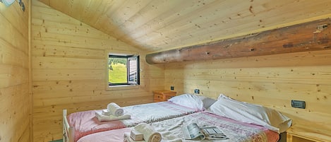 Una habitación tipo cabaña de madera con dos camas, una ventana y techo de madera.