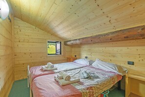 Ein Zimmer in einer Holzhütte mit zwei Betten, einem Fenster und einer Holzbalkendecke.
