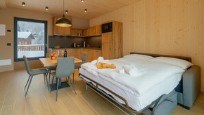 A modern room with a bed, a dining table, and chairs. There is a window with a view of a snowy landscape. - Leba 3 (Livigno)