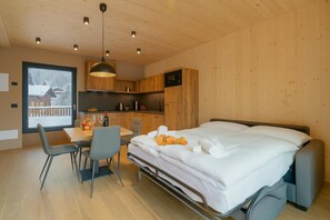 Een moderne kamer met een bed, een eettafel en stoelen. Er is een raam met uitzicht op een besneeerd landschap.