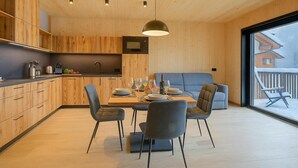 A modern kitchen with wooden cabinetry, a dining area with a table set for four, and a large window with a view of a snowy landscape. - Leba 3 (Livigno)