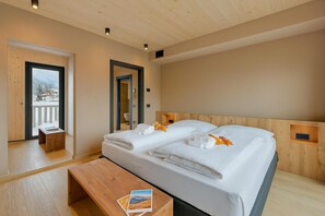 A modern hotel room with two beds, wooden headboards, a wooden bench, and a small table with a book. - Leba 3 (Livigno)