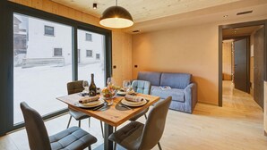 A dining area with a wooden table set for four, a sofa, and a view of the street outside. - Leba 2 (Livigno)