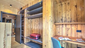 Ein modernes Zimmer mit Holzwänden und einem eingebauten Schreibtisch mit Stuhl. Ein roter Koffer steht auf einem Regal, und auf dem Schreibtisch liegen Bücher.
