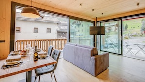 Ein moderner Essbereich mit einem Holztisch, gedeckt für eine Mahlzeit, einer Couch und einem großen Fenster mit Blick auf eine Berglandschaft.