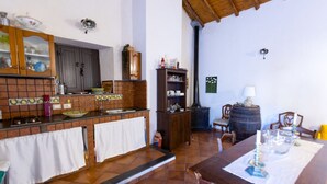 A kitchen with a tiled backsplash, wooden cabinets, a stove, and a dining area with a table set for two. - Vigna dell`Etna - Piedimonte Etneo (Piedimonte Etneo)