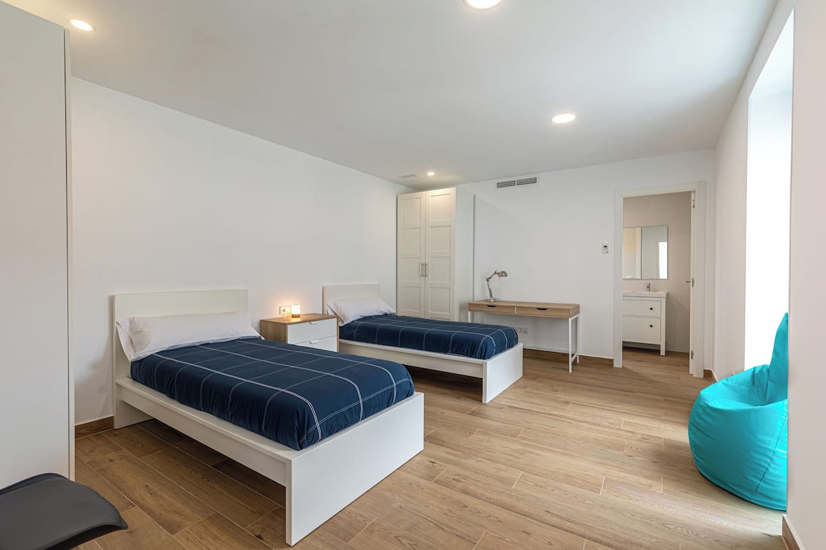 A modern bedroom with two beds, a desk, and a chair.