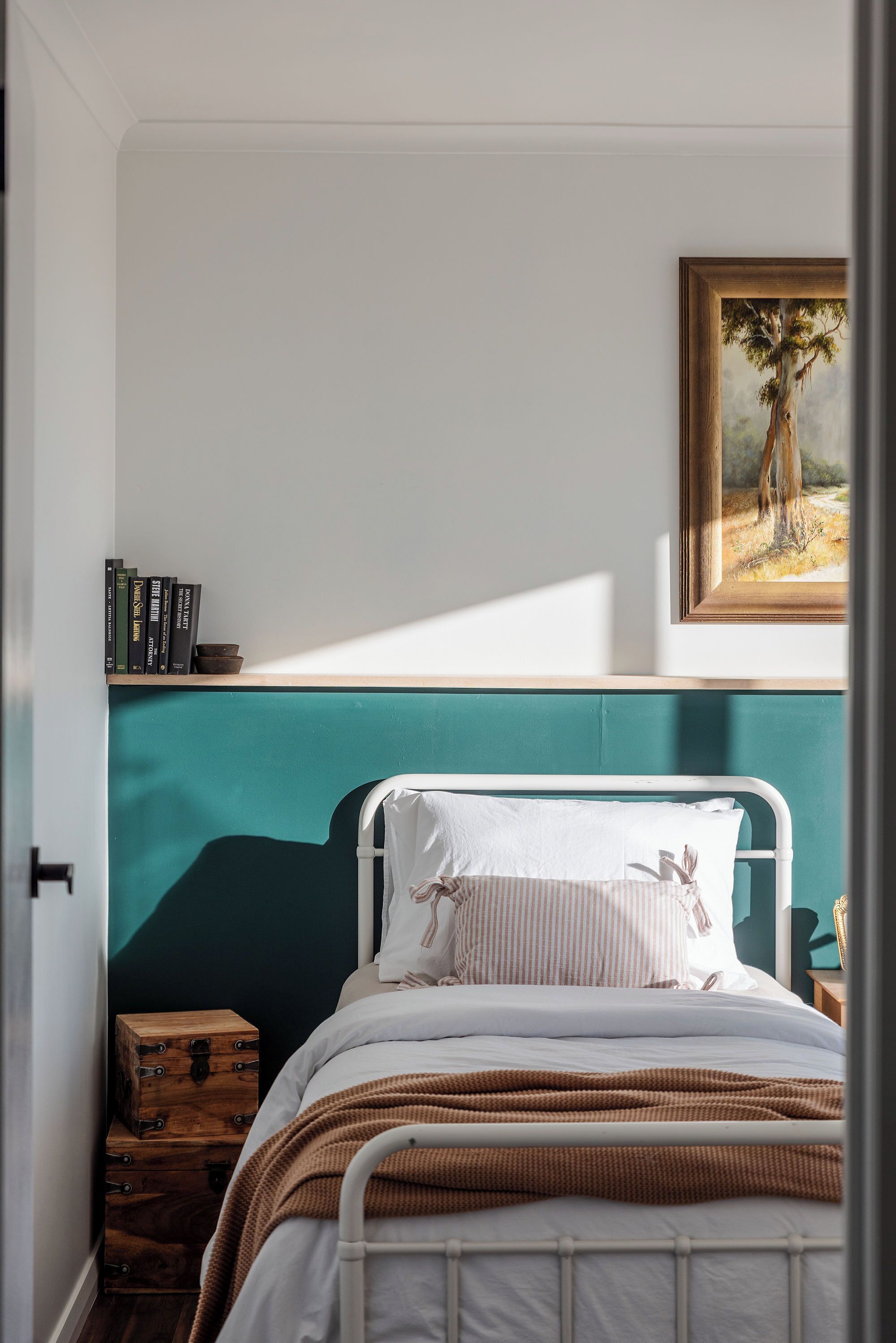Un dormitorio con una cama, un cabecero color turquesa, un cuadro enmarco y cajas de almacenamiento de madera.