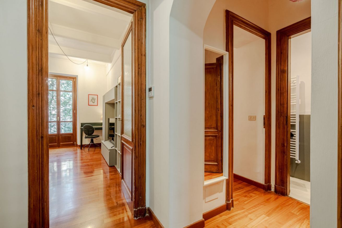 A hallway with wooden flooring, a desk with a chair, and a radiator.