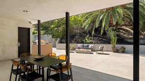 A modern outdoor dining area with a table and chairs, a fire pit, and a seating area with a sofa and cushions. - Valea Estate - Secluded Beverly Hills Retreat 1-acre Oasis (Beverly Hills)