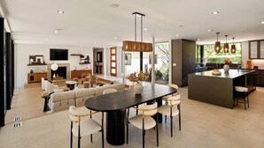 A modern open-plan living and dining area with a large oval table, comfortable seating, and a kitchen island. - Valea Estate - Secluded Beverly Hills Retreat 1-acre Oasis (Beverly Hills)
