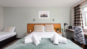 Habitación de hotel con cama, dos mesitas de noche, un escritorio, una silla, ventana con cortinas y un cuadro colgado en la pared.