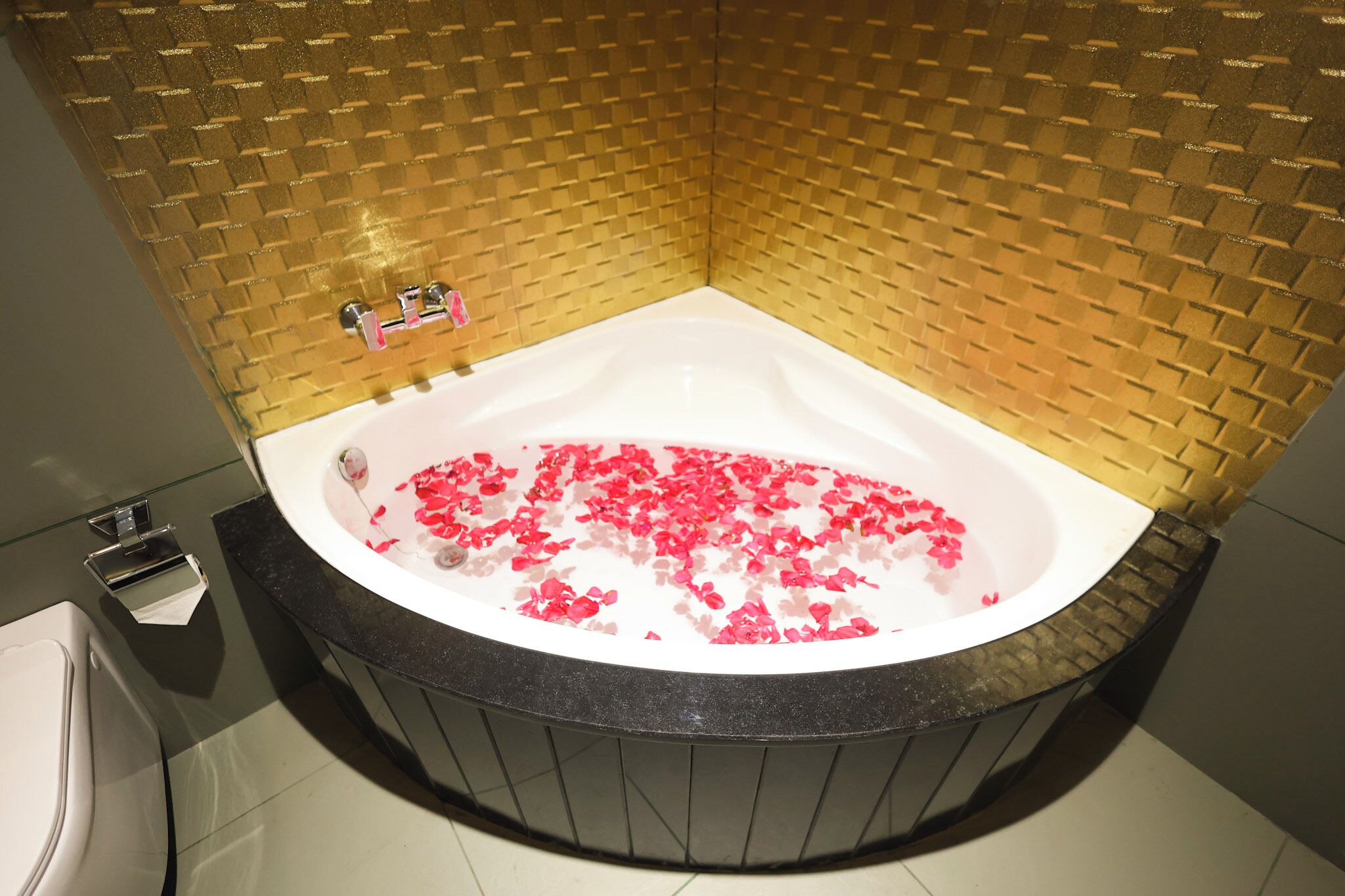 A bathroom with a freestanding bathtub filled with water and rose petals, a toilet, and a shower area.