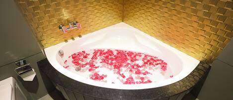 A bathroom with a freestanding bathtub filled with water and rose petals, a toilet, and a shower area.