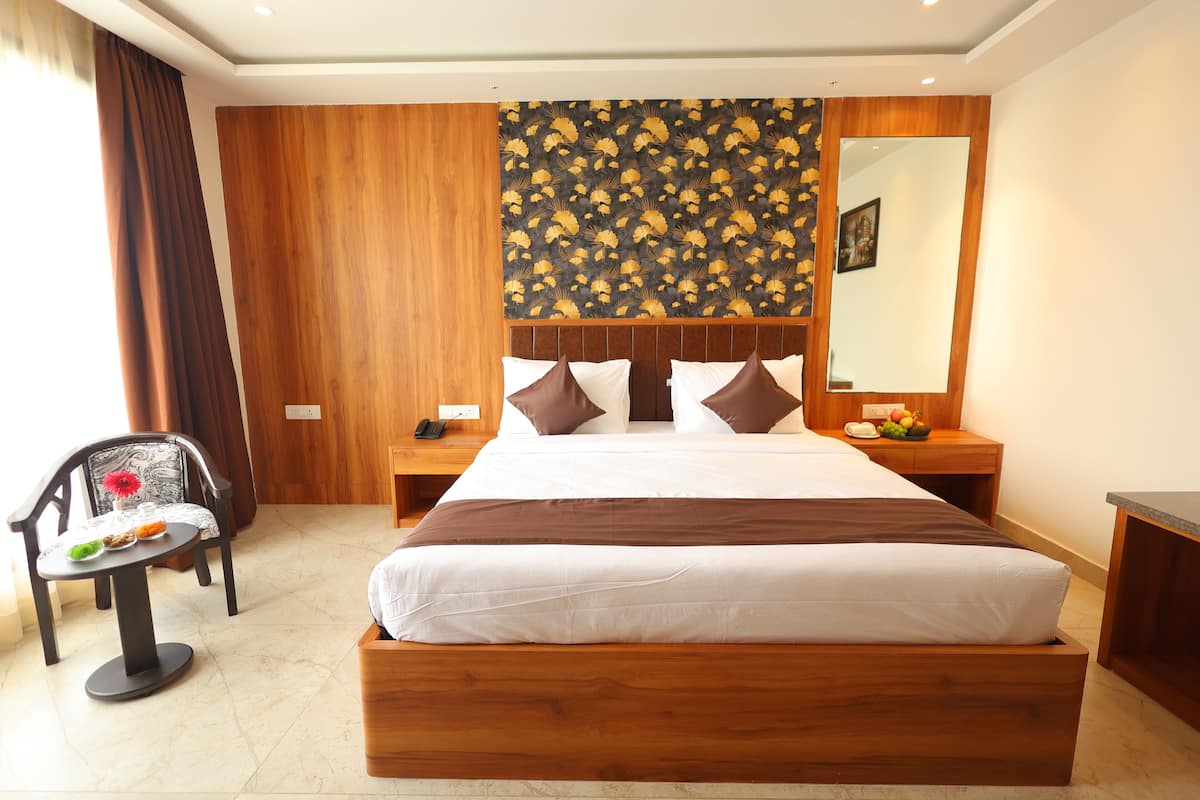 Une chambre d’hôtel avec un grand lit, une tête de lit en bois, une table de chevet avec un téléphone, une chaise avec une petite table, et un miroir au mur.
