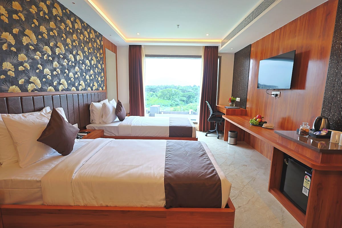 Une chambre d’hôtel avec deux lits, un bureau avec une télévision et une vue sur la verdure.