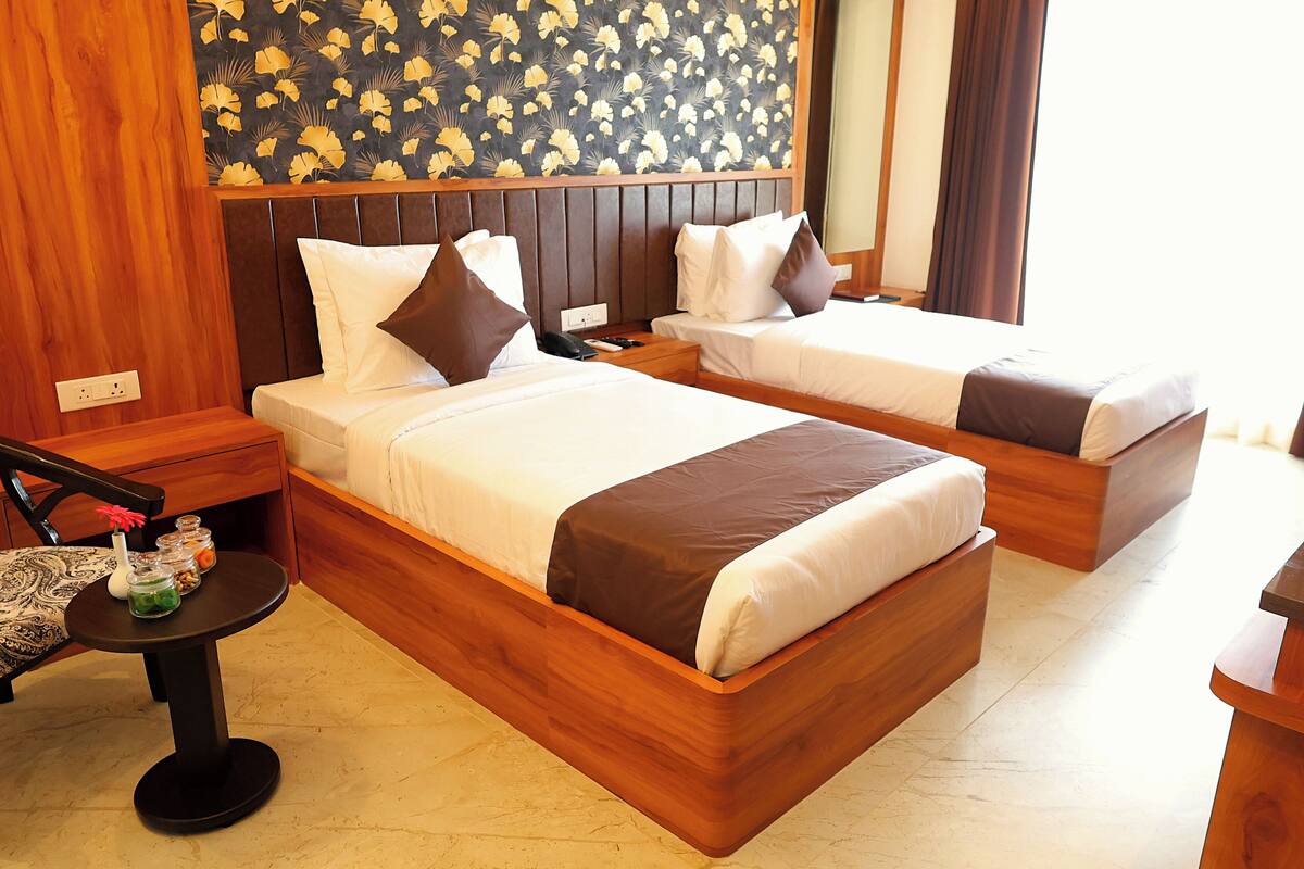 Une chambre d’hôtel avec deux lits en bois, une petite table sur laquelle est posé un vase, et une chaise à motifs.