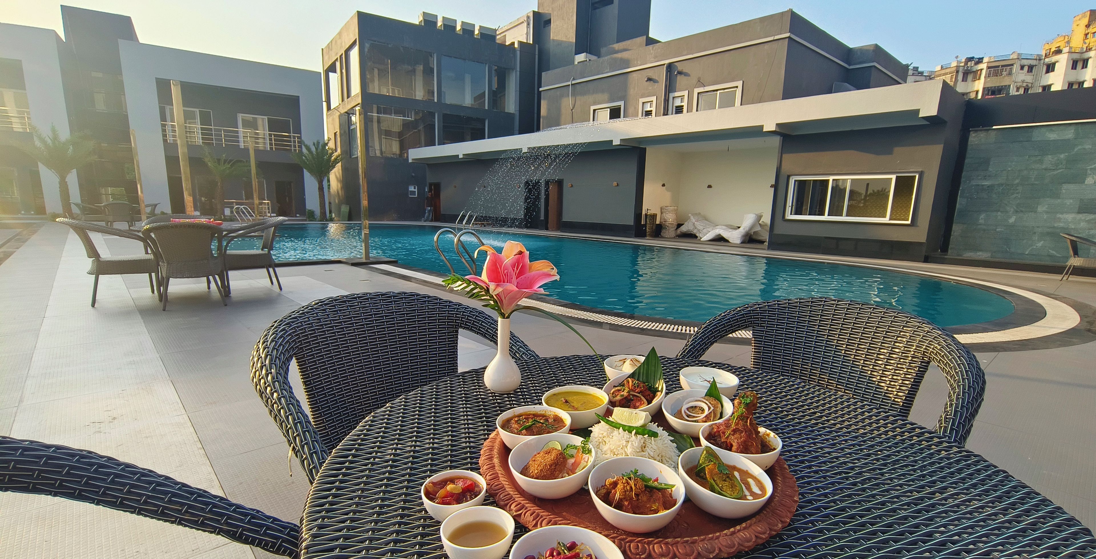 A dining table with various dishes, a pool, and modern buildings in the background.