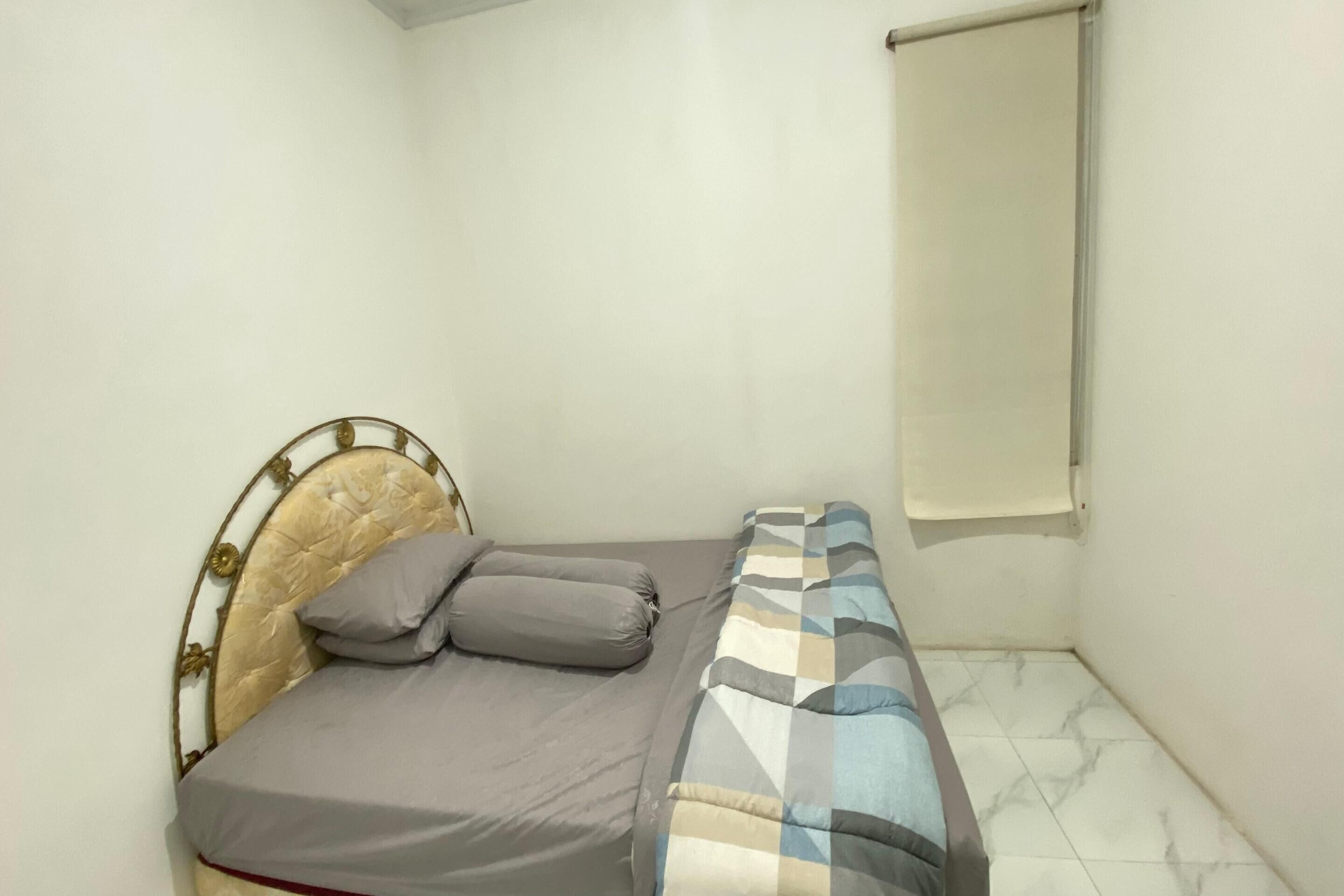 Habitación pequeña con cama individual, cabecera de metal, ropa de cama gris y manta a cuadros.